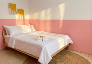 A single bed with a white mattress and pillows, a wooden frame, and a woven rug on a tiled floor.