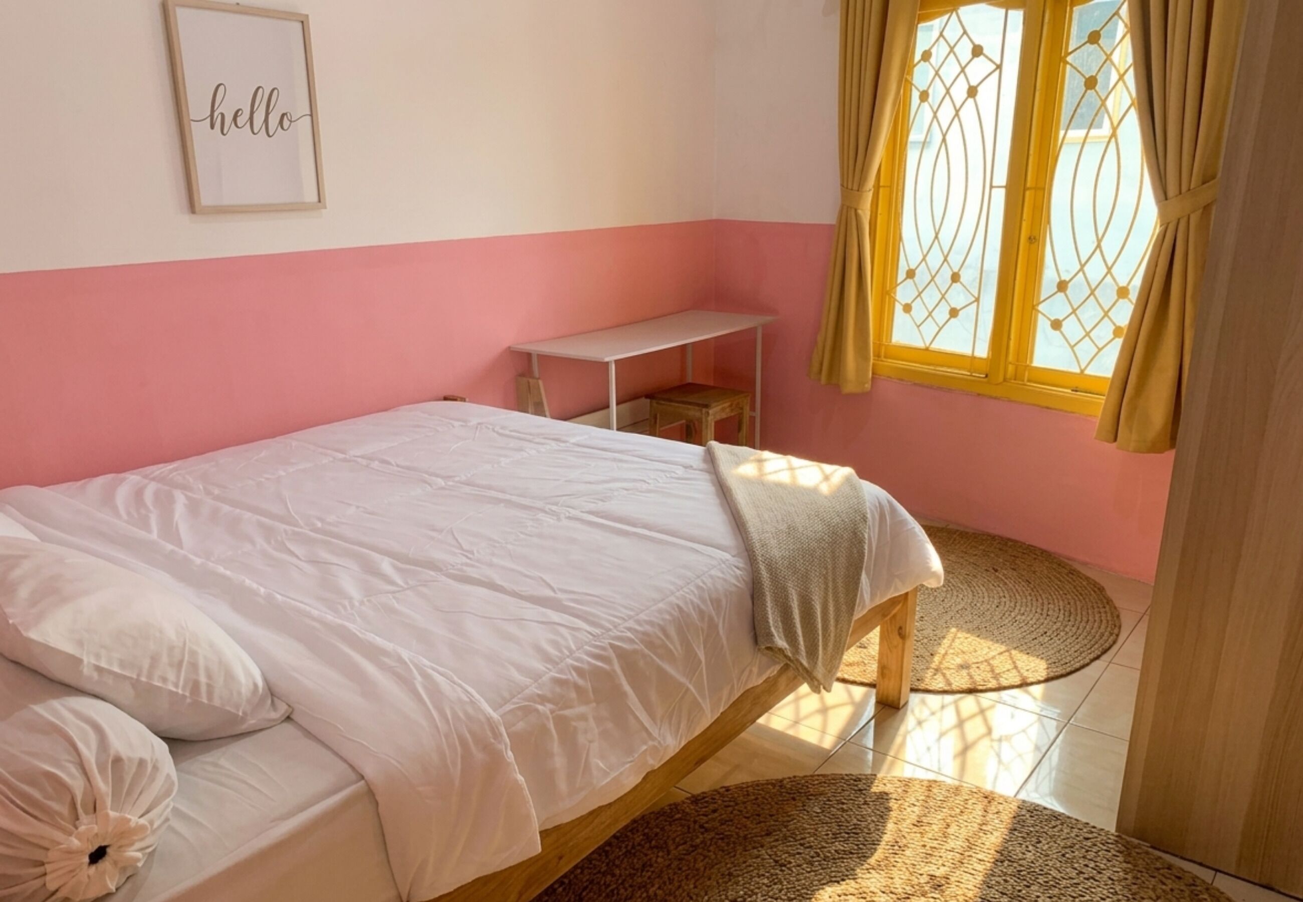 Habitación con una cama individual, una mesita blanca pequeña, una cortina amarilla y un cuadro con la palabra 'hello' en la pared.