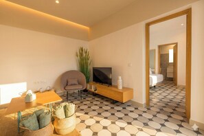 Ein modernes Hotelzimmer mit Fernseher, einer Sitzecke und Blick ins Bad.