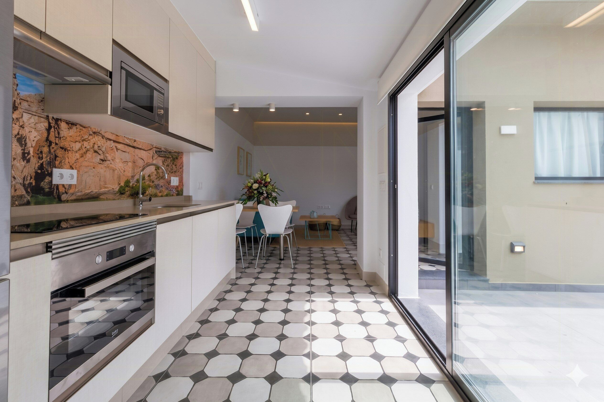 A modern kitchen with a stone backsplash, stainless steel appliances, and a dining area with a hexagonal tile floor.
