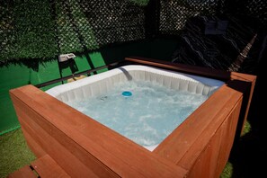 Ein Whirlpool mit Holzrahmen, umgeben von einer grünen Hecke und einer Holzterrasse.
