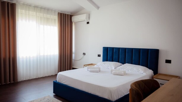 Quarto de hotel com cama, escrivaninha, cadeira, janela com cortinas e ar condicionado.