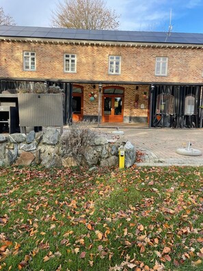 Een bakstenen gebouw met een stenen muur, een overdekte ingang en een verhard gebied bezaaid met herfstbladeren.