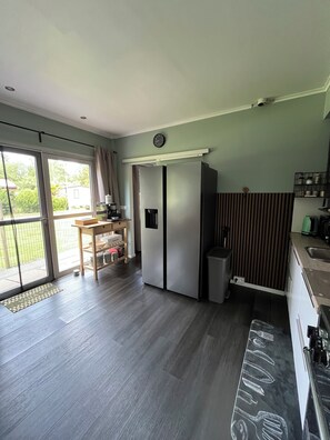 A kitchen with a refrigerator, a sink, and a dining area with a table and chairs. - Cozy little chalet for a family of up to 4 people and their little rascals (Lanaken)