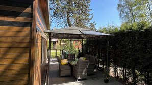 Una zona patio con tavolo e sedie, un'area salotto coperta e vista su un albero alto.