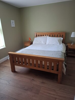Een slaapkamer met een houten bed, een nachtkastje met een lamp en een raam met jaloezieën.