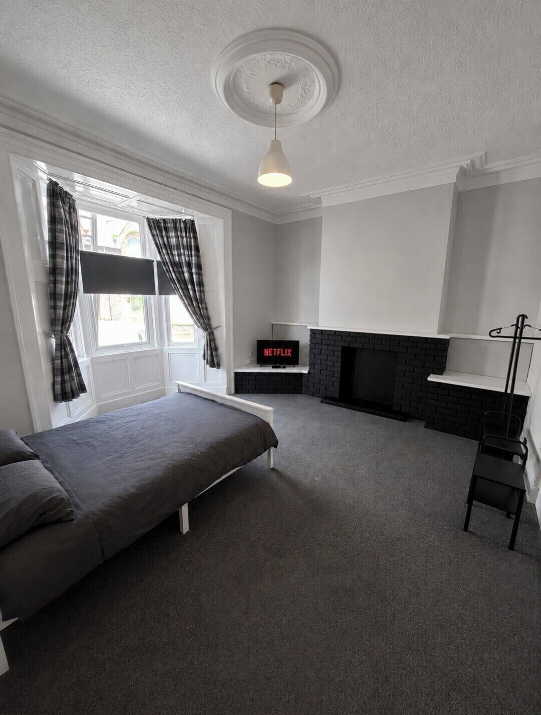 A room with a bed, a fireplace, a TV, and a window with curtains.