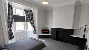 A room with a bed, a fireplace, a TV, and a window with curtains. - Alice Place (Sunderland)