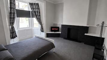 A room with a bed, a fireplace, a TV, and a window with curtains.