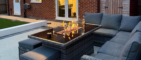 A patio with a glass-top table, wicker furniture, and a brick house in the background.