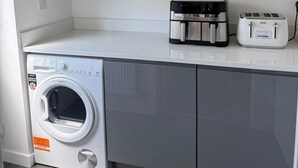 A compact laundry area with a front-loading washing machine, a small refrigerator, and a toaster on a white countertop. - House Sleeps 6 With Parking and Garden (Liverpool)