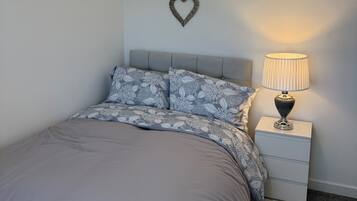 Quarto com cama, mesa de cabeceira, abajur, decoração em formato de coração e luminária de teto aconchegante.