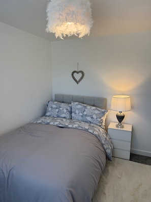A bedroom with a bed, a nightstand, a lamp, a heart-shaped decoration, and a fluffy ceiling light fixture.