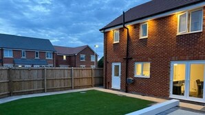 A residential backyard with a well-maintained lawn, a wooden fence, and a brick house with a door and windows. - House Sleeps 6 With Parking and Garden (Liverpool)