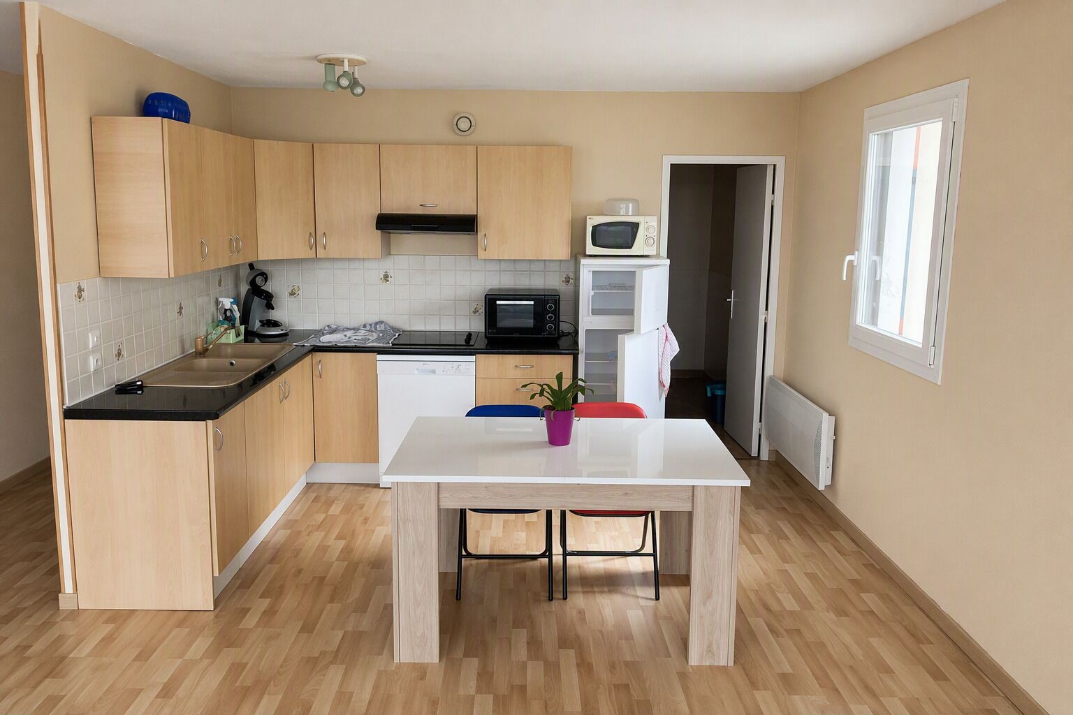 Une cuisine compacte avec des meubles en bois, un plan de travail noir, une table blanche et une plante en pot.