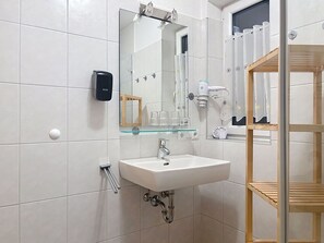 Ein Badezimmer mit einem weißen Waschbecken, einer Glasablage, einem Spiegel, einem Händetrockner und einem Handtuchhalter.