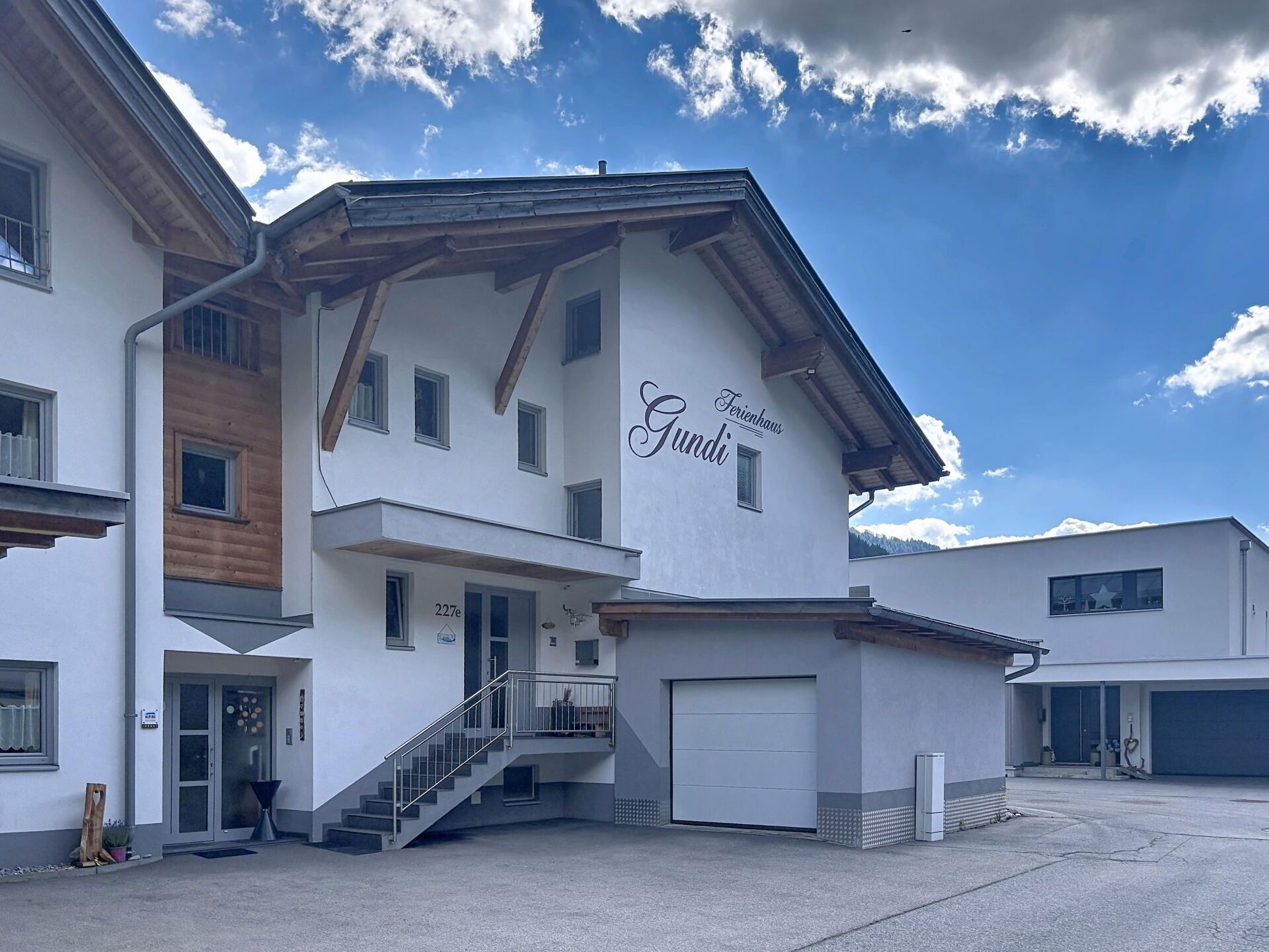 Een modern gebouw met een bord waarop 'Ferienhaus Gundi' staat en een trap naar de ingang.