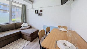 Ein modernes Wohnzimmer mit einer Couch, einem Esstisch für zwei Personen und einem an der Wand montierten Fernseher.