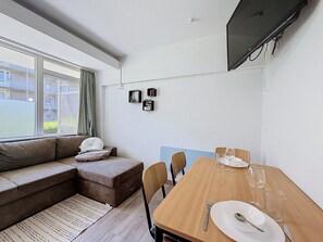 Ett modernt vardagsrum med en soffa, ett matbord för två personer och en tv som är monterad på väggen.