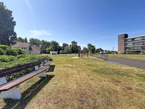 Ein Park mit einem Spielplatz, einer Bank und Gebäuden im Hintergrund.