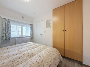 Ett sovrum med en säng, en garderob, ett fönster med gardiner och ett element.