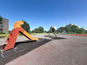Ein Spielplatz mit einer großen, orangefarbenen Kletteranlage und einem Basketballplatz.
