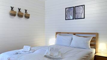 Een net opgemaakt bed met witte lakens en handdoeken, een houten hoofdbord en een nachtkastje met een lamp.