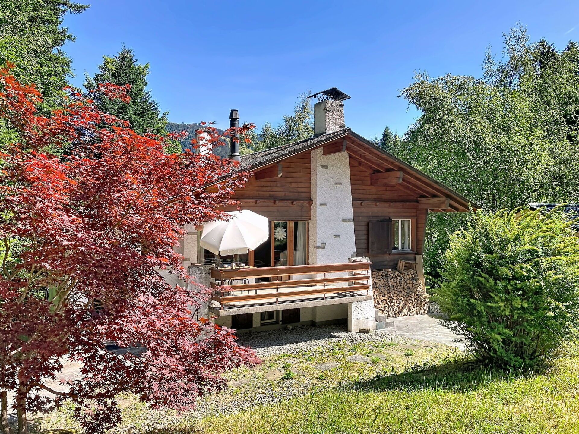 Een chalet met een houten terras, een overdekte zithoek en een stenen schoorsteen.