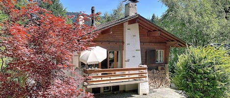 Una cabaña con terraza de madera, un espacio de descanso cubierto y una chimenea de piedra.