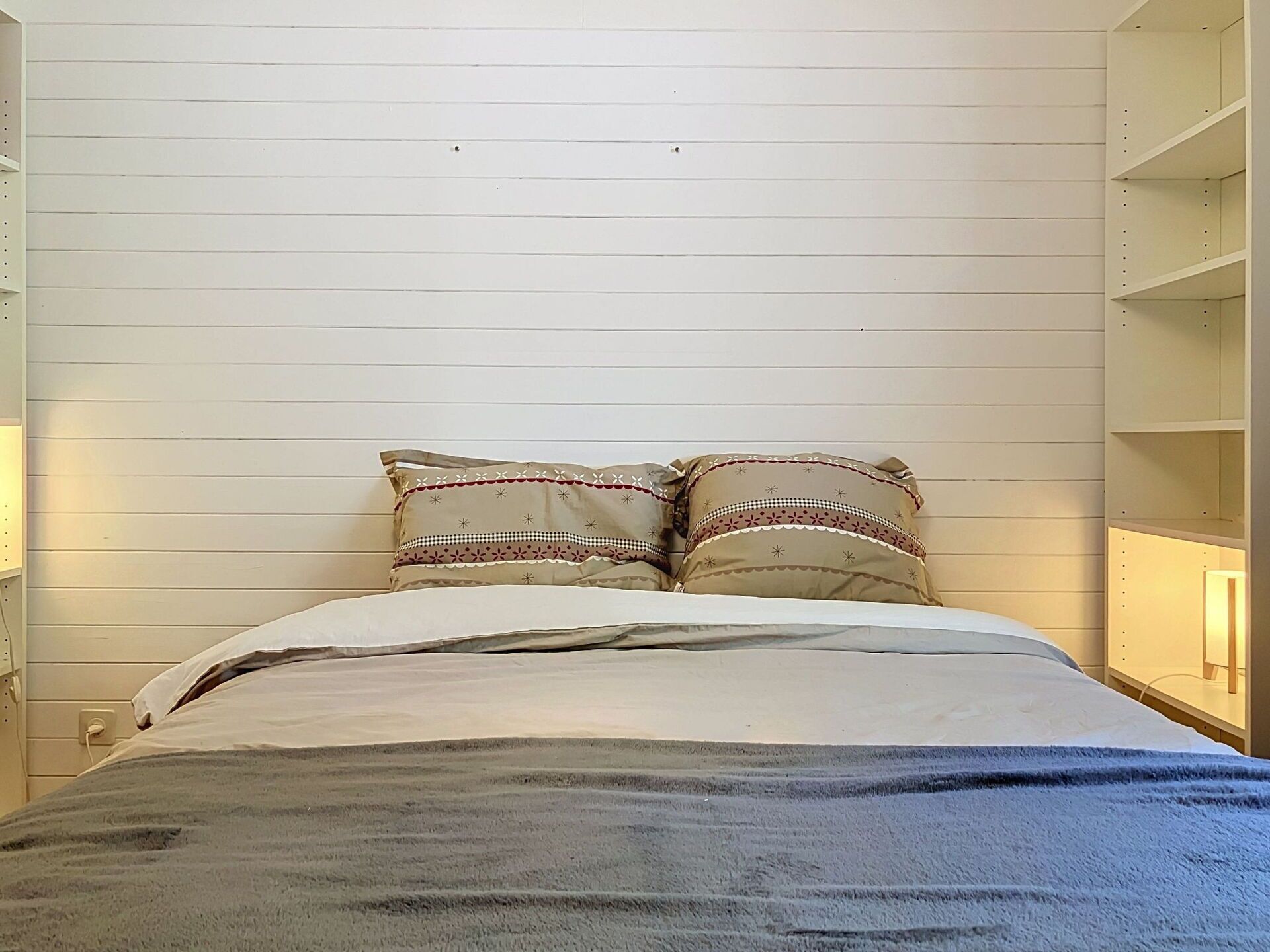 Ein Bett mit zwei Zierkissen, einem weißen Kopfteil und einem Nachttisch mit einer Lampe.