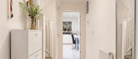 A hallway with a radiator, a mirror, a staircase, and a door leading to a kitchen area.