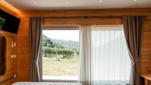 Un dormitorio con cama, paredes de madera, televisor y un ventanal con cortinas.