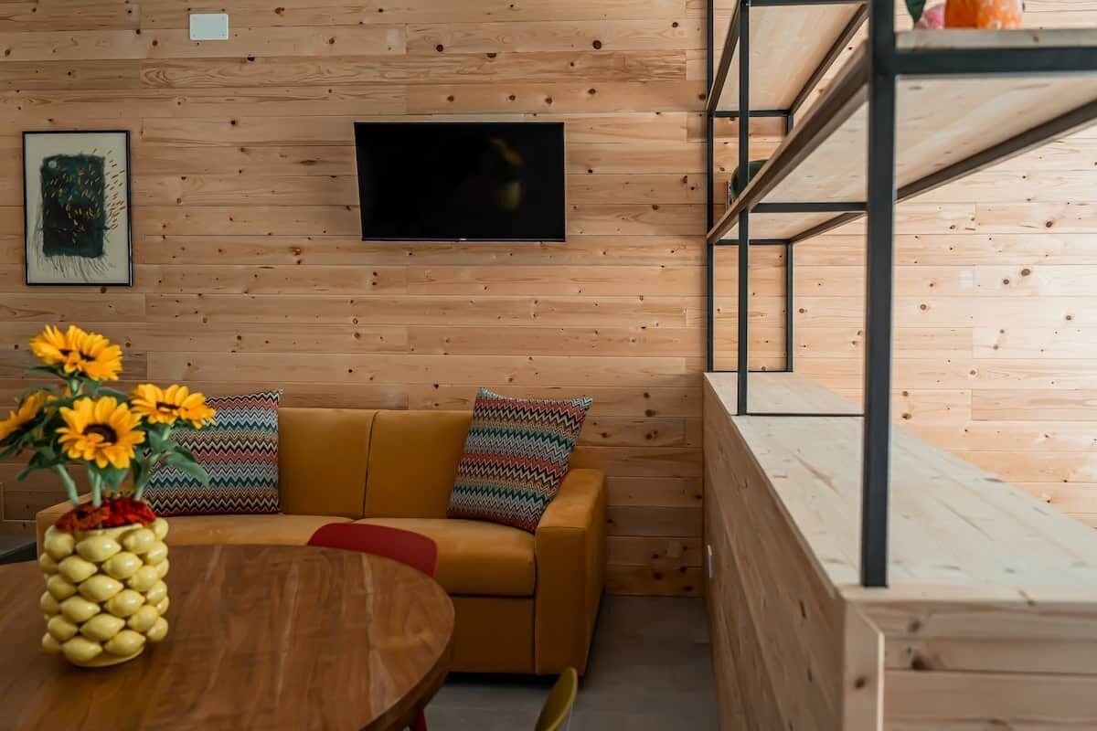 Ein Zimmer mit Holzwand, einer Couch mit gemusterten Kissen, einem Flachbildfernseher und einem Holztisch mit einer ananasförmigen Vase.