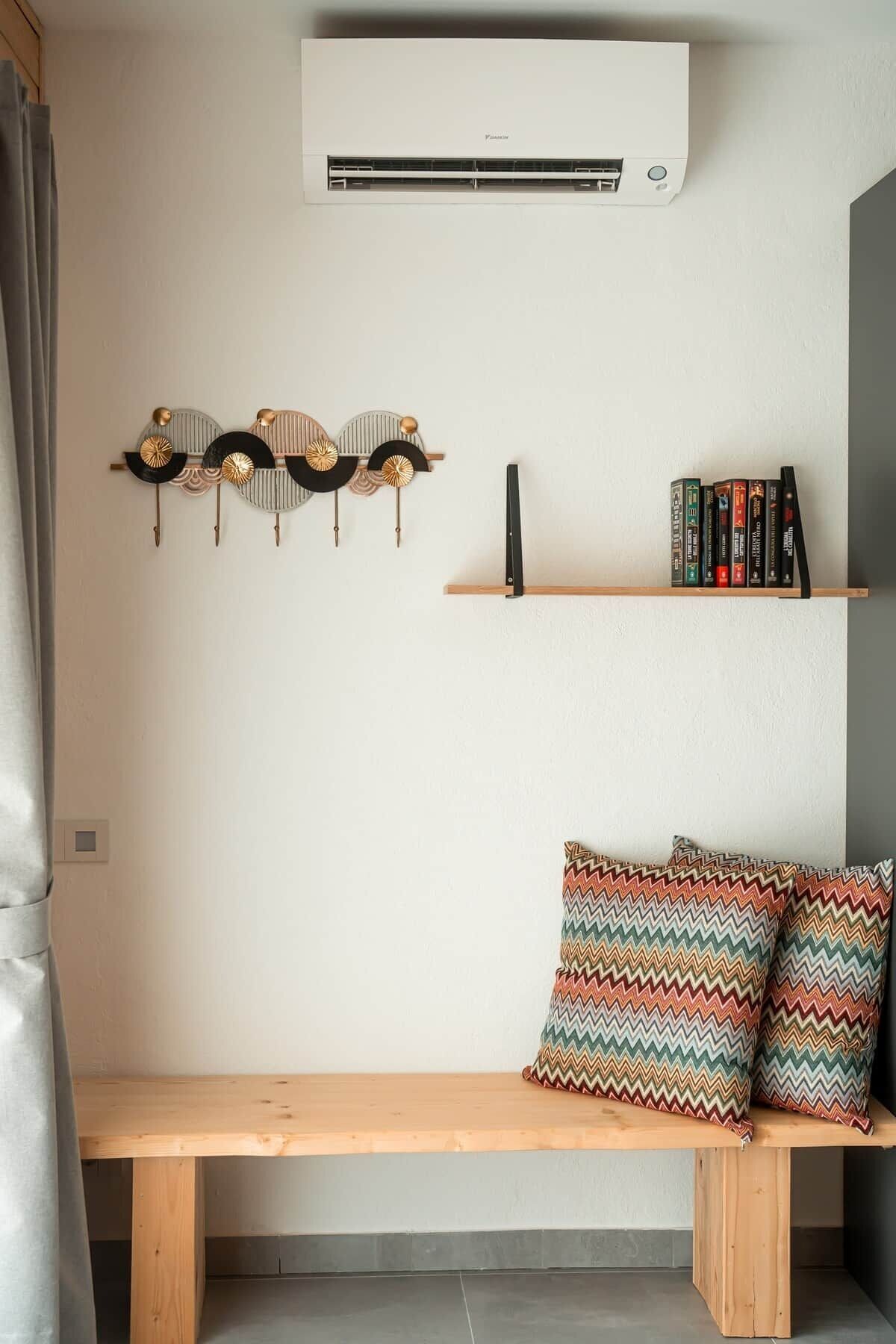 Ein Zimmer mit einer Holzbank, einer Wandklimaanlage, einem Wanddekor und einem Bücherregal.