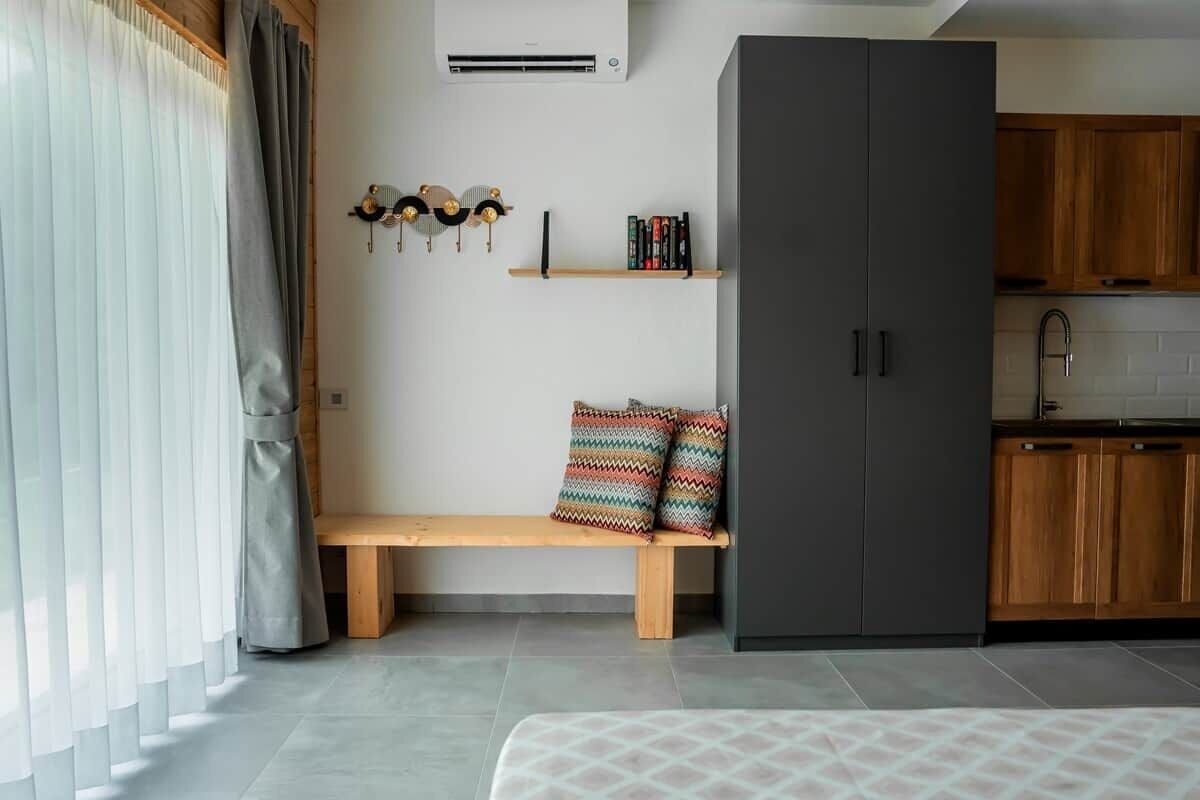 Une chambre moderne comprenant un lit, un banc, une armoire, une étagère avec des livres et un coin cuisine.