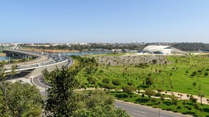 A modern urban landscape with a prominent white stadium, a curved highway, and a body of water.