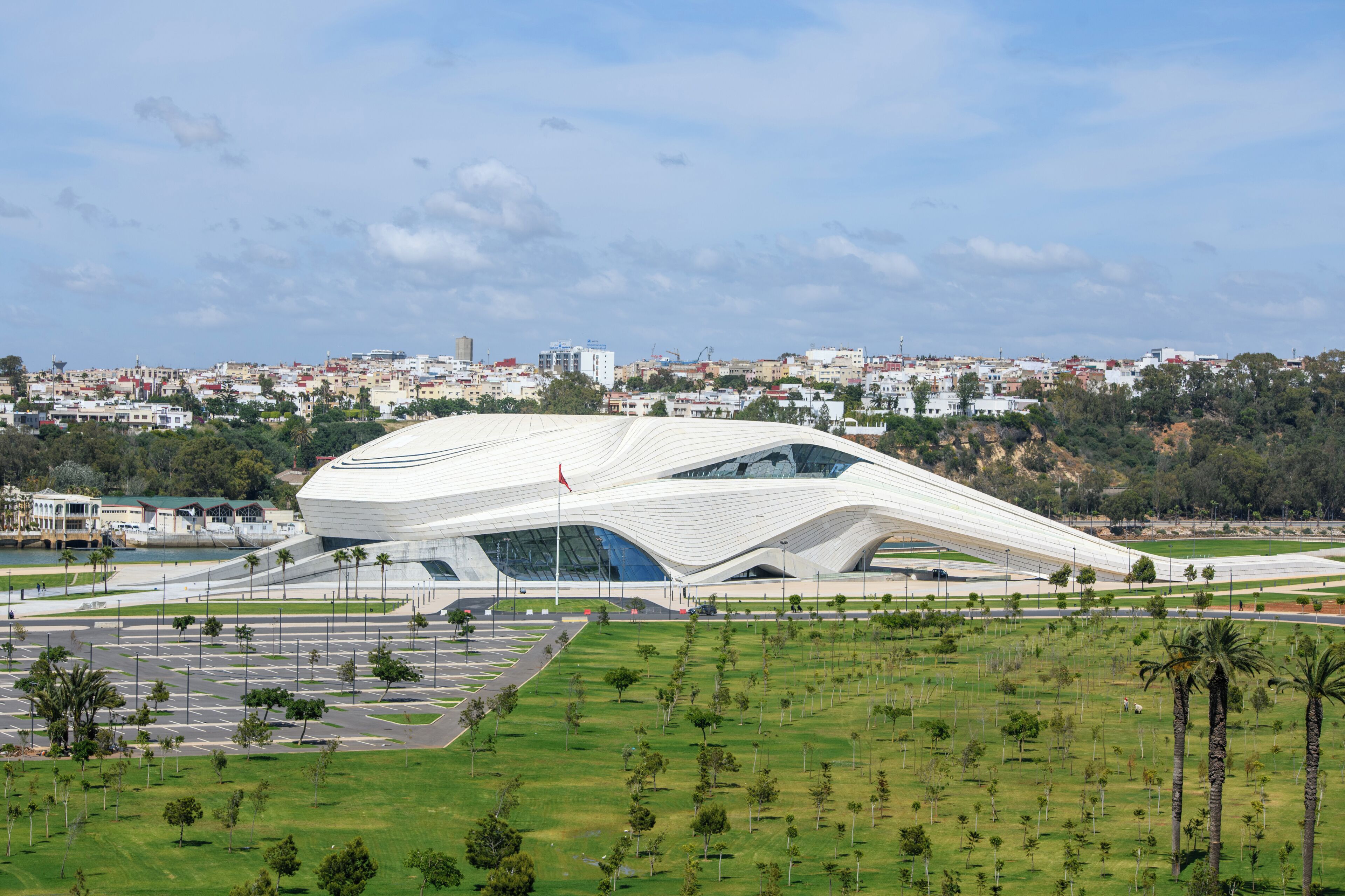 Edificio de arquitectura moderna con un diseño curvo único, rodeado de un parque bien cuidado y un paisaje urbano al fondo.