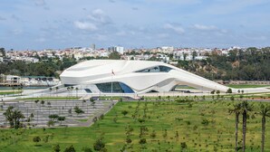 A modern architectural building with a unique curved design, surrounded by a well-maintained park and a cityscape in the background.