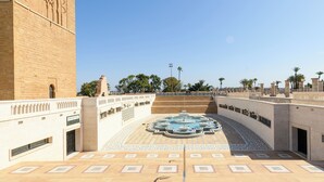 A courtyard with a fountain, steps leading up to a building, and palm trees in the background.
