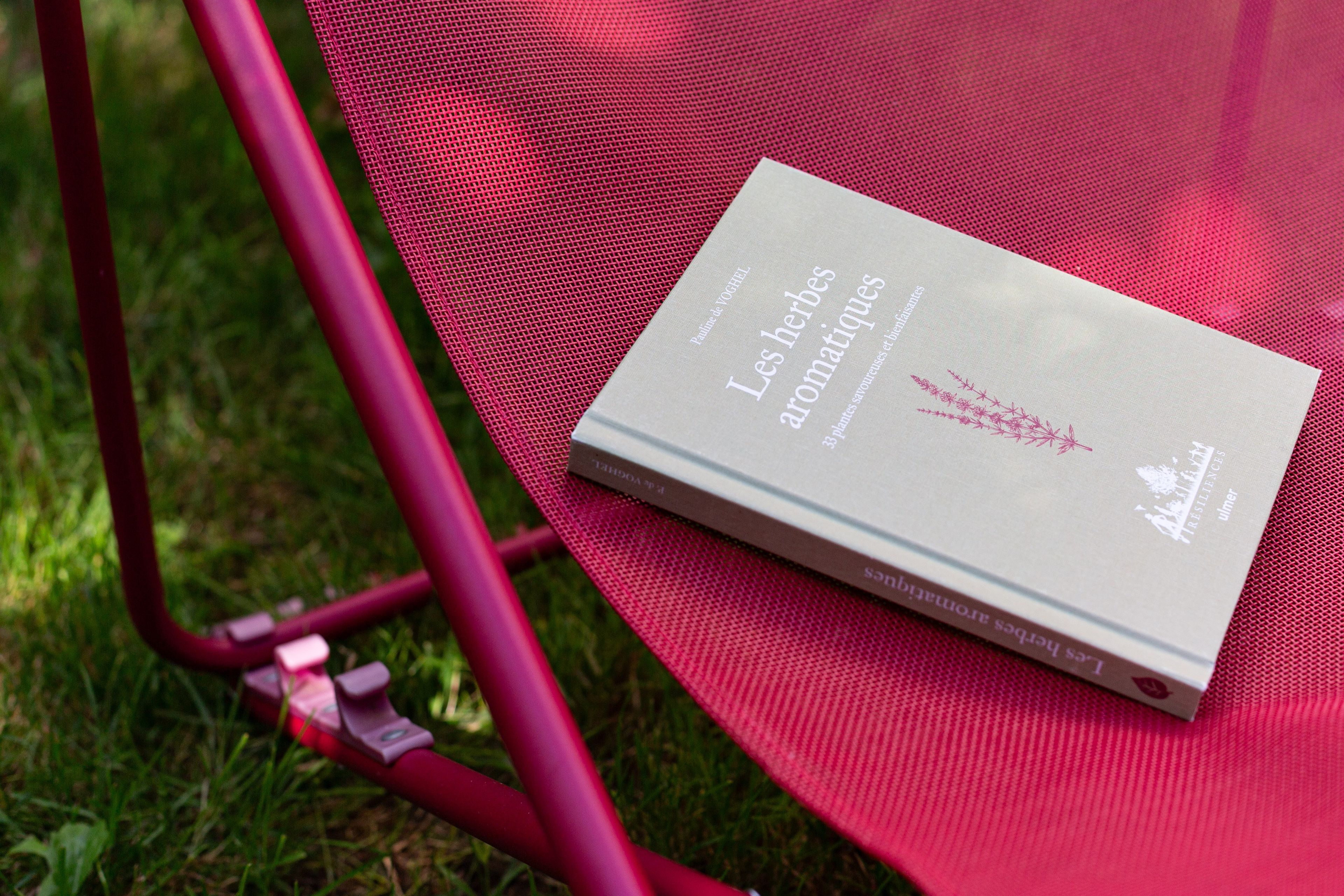 A book titled 'Les herbes aromatiques' placed on a red mesh chair outdoors.