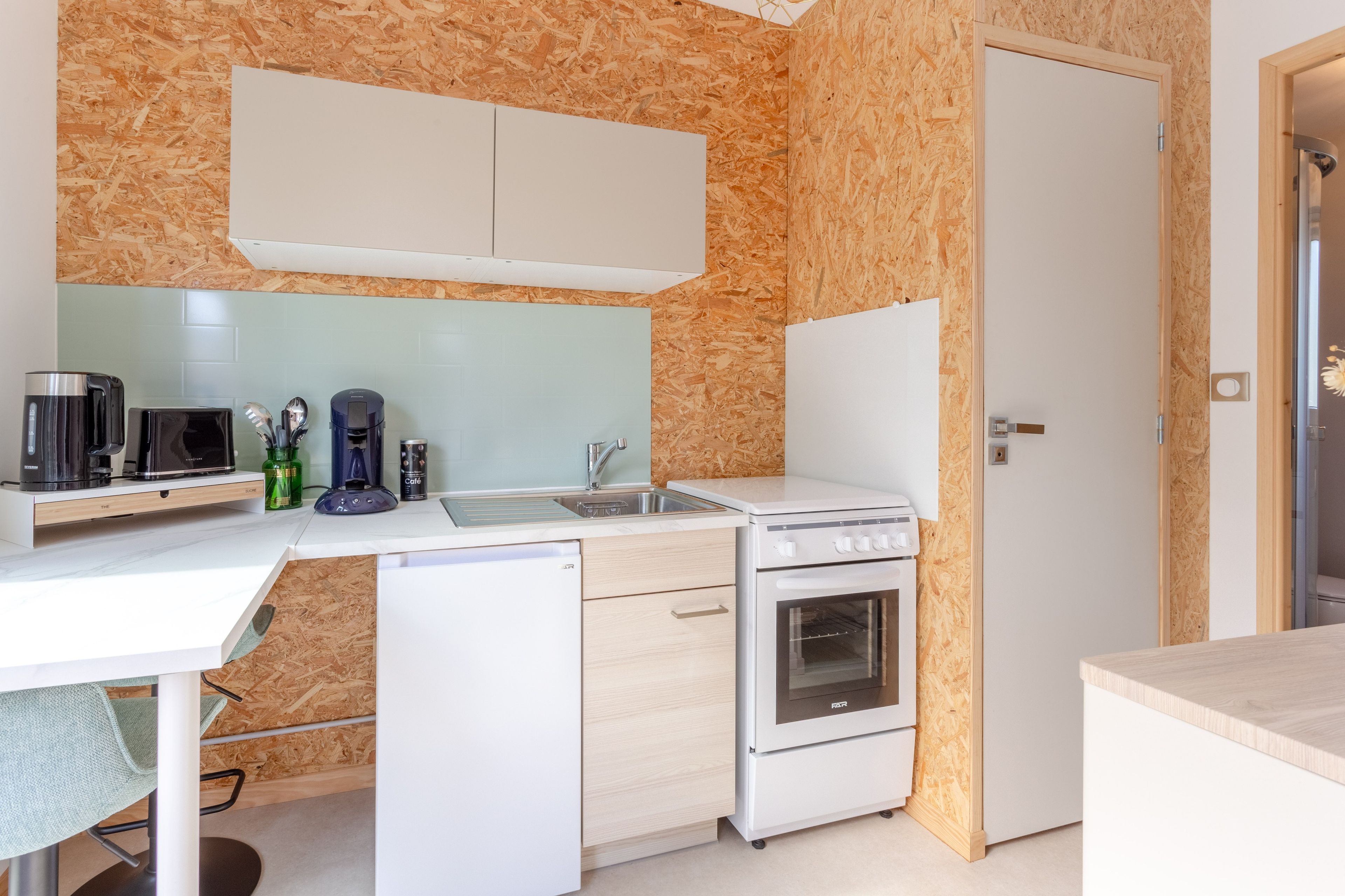 Una cucina compatta con forno a microonde, macchina del caffè e piccolo frigorifero.