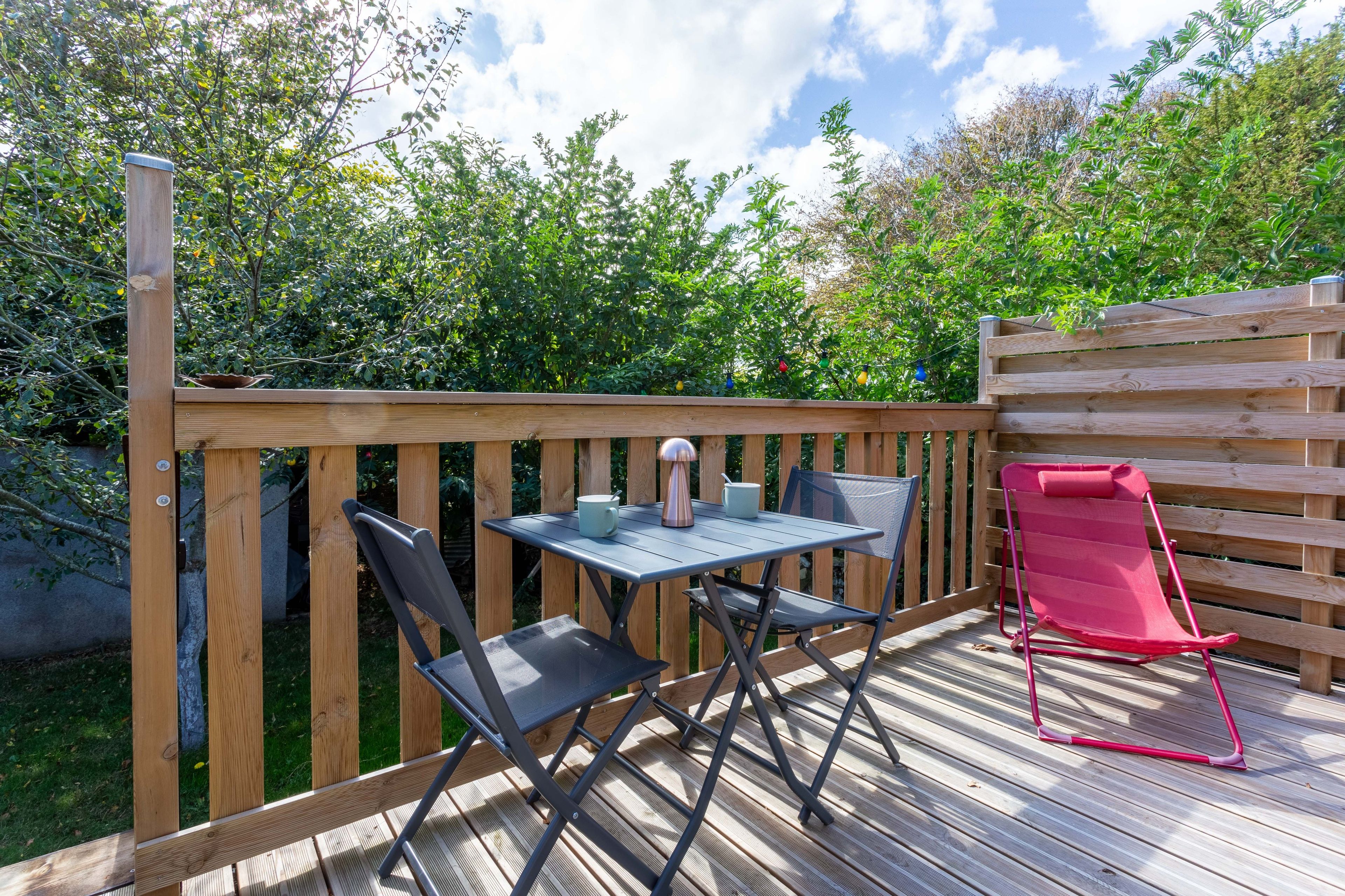 An outdoor deck with a table and chairs, surrounded by a wooden fence and greenery.