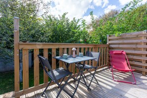 An outdoor deck with a table and chairs, surrounded by a wooden fence and greenery.