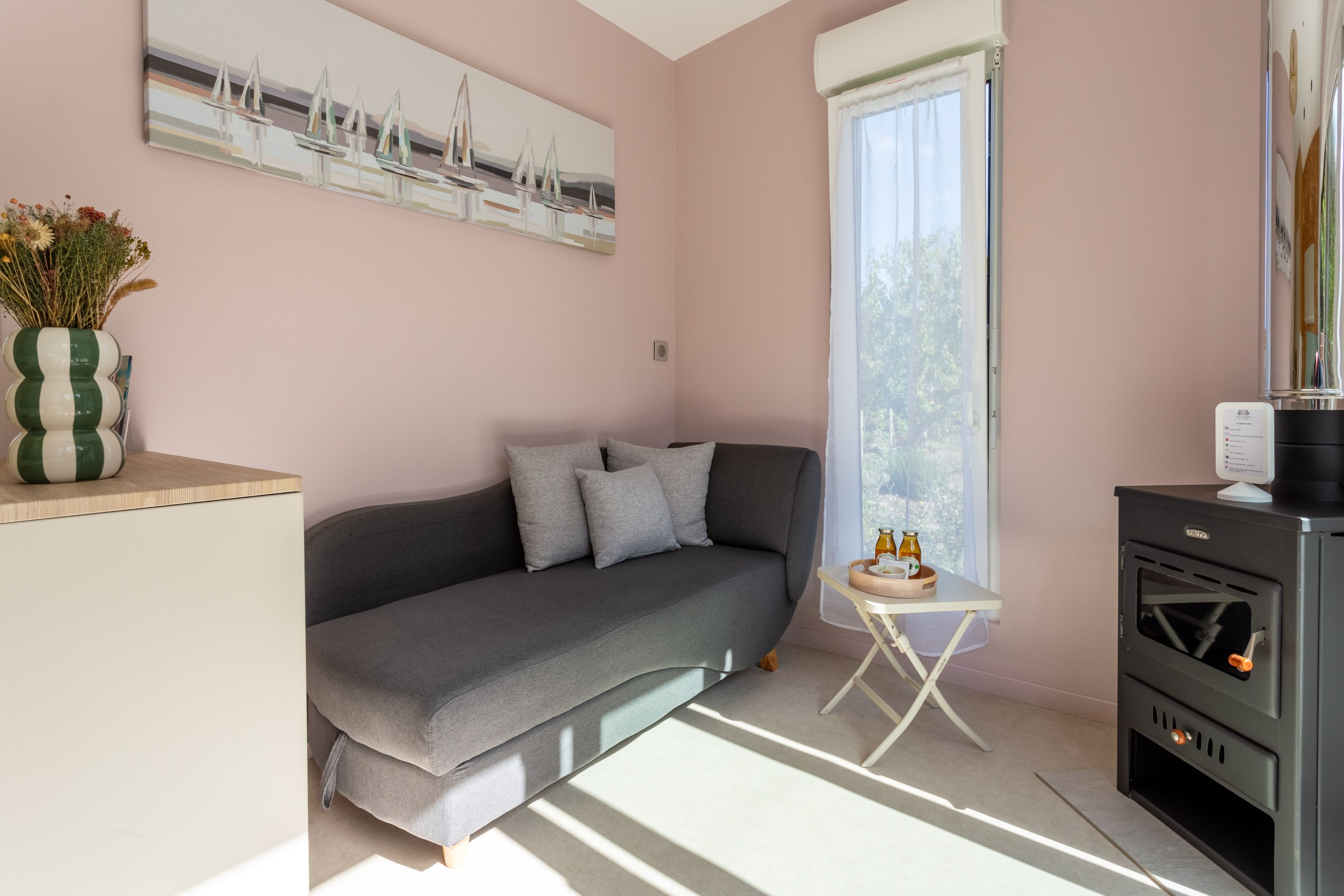 Un salon moderne avec un canapé gris, une petite table d’appoint sur laquelle se trouve une bouteille, et un climatiseur fixé au mur.