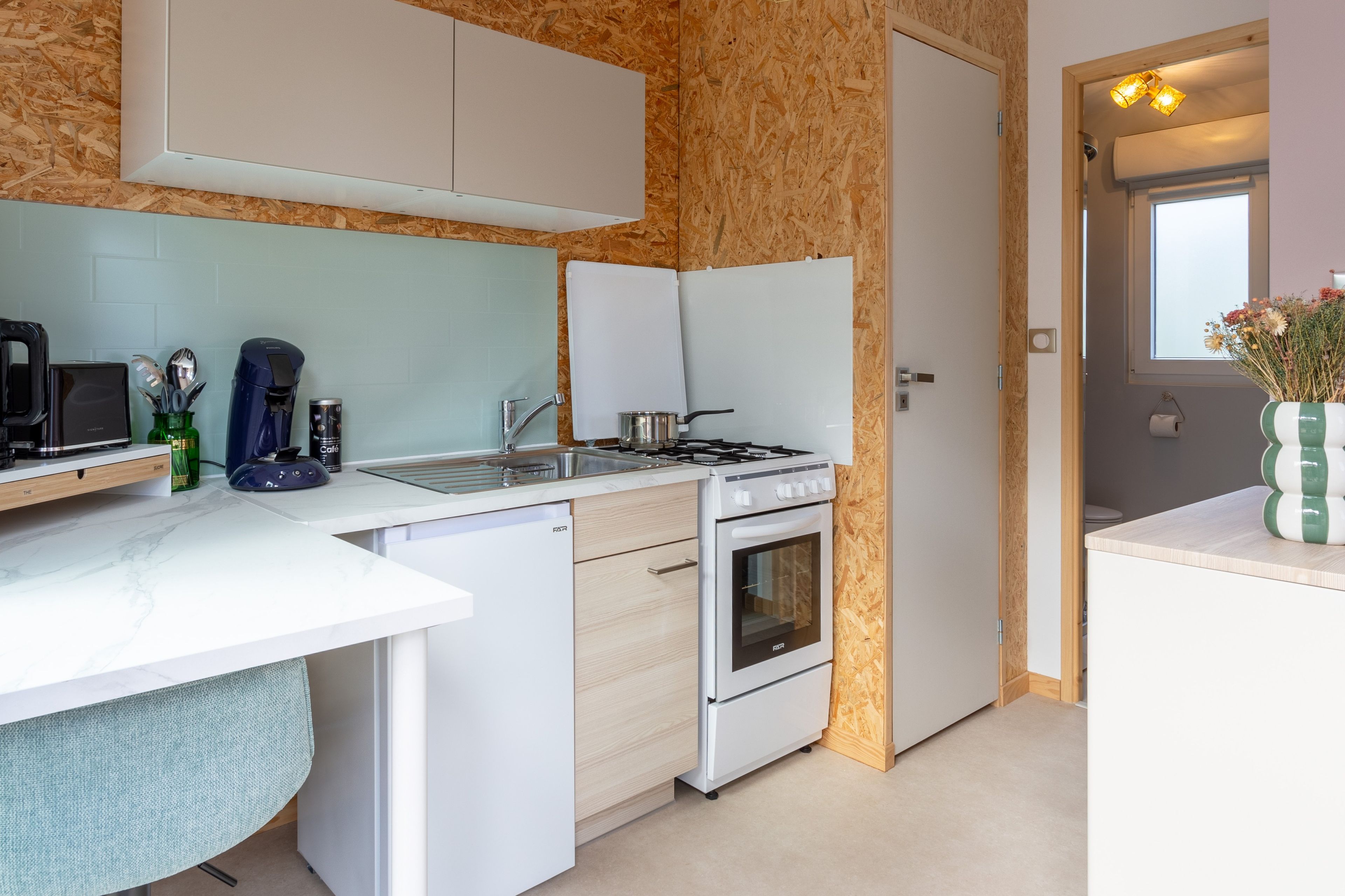 Une cuisine compacte avec un plan de travail blanc, un four encastré, une cuisinière et un évier.