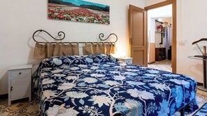 Una camera da letto con un letto, un comodino, una cassettiera, un quadro appeso al muro e una porta che dà su un'altra stanza.