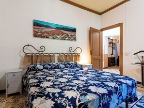 Ein Schlafzimmer mit Bett, Nachttisch, Schminktisch, einem Bild an der Wand und einer Tür zu einem anderen Raum.