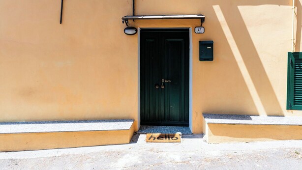 Un edificio con una porta verde scuro, una piccola cassetta postale e una targa con il numero sopra la porta.