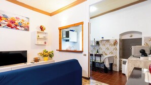 Un soggiorno con un divano blu, una TV a schermo piatto, un quadro e un piccolo scaffale con oggetti decorativi.