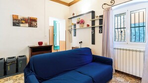 Una stanza con un divano blu, soffitto in legno, termosifone e una finestra con inferriate.